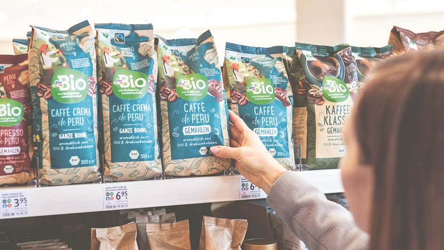Eine Frau greift nach einer Kaffeepackung in einem Verkaufsregal.
